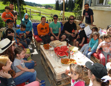 Viele Menschen sitzen im Freien auf selbstgemachten Holzpaletten Sofas. in der Mitte befindet sich ein Holztisch mit verschiedenen Häppchen.