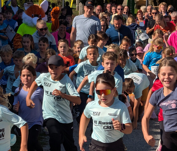 Viele Kinder starten gemeinsam zu einem Lauf, Zuschauer*innen säumen die Strecke.