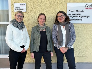Drei Frauen stehen vor einer gelben Hauswand und lächeln in die Kamera