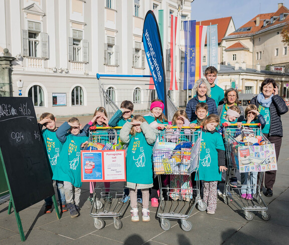 Kinder mit Betreuer*innen präsentieren gesammelte Waren bei der Aktion „Kilo gegen Armut“ in Klagenfurt.