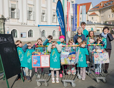Kinder mit Betreuer*innen präsentieren gesammelte Waren bei der Aktion „Kilo gegen Armut“ in Klagenfurt.