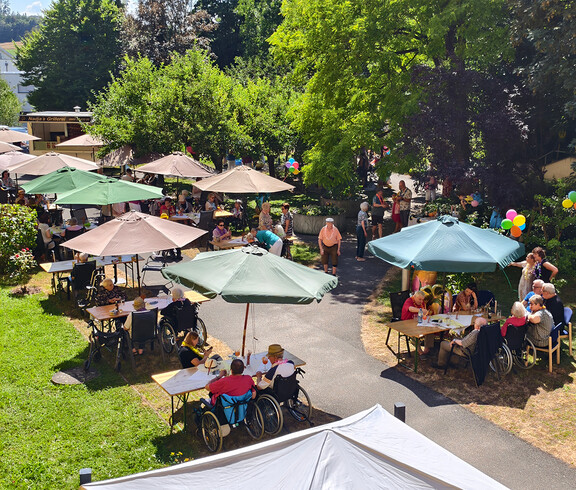 Viele Sonnenschrime mit Bänken und Tischen darunter auf denen Menschen sitzen.