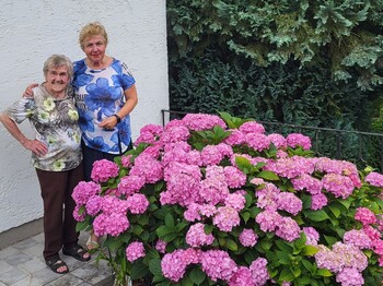 Zwei ältere Damen lins im Bild, rechts davor schöne rosa blühende Stauden.