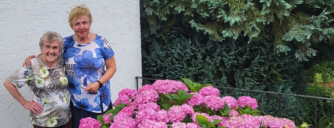 Zwei ältere Damen lins im Bild, rechts davor schöne rosa blühende Stauden.