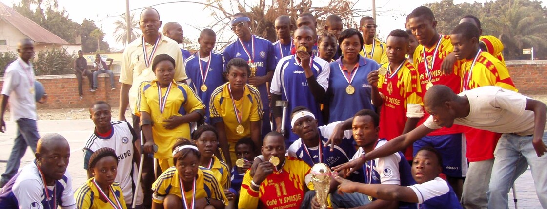 Gruppe von Sportlerinnen und Sportlern mit Behinderungen in Sportkleidung zeigt stolz Medaillen und Pokale nach einem Turnier in der Demokratischen Republik Kongo.