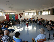 Bewohner*innen sitzen im Kreis, Adventkranz auf rotem Tuch in der Mitte