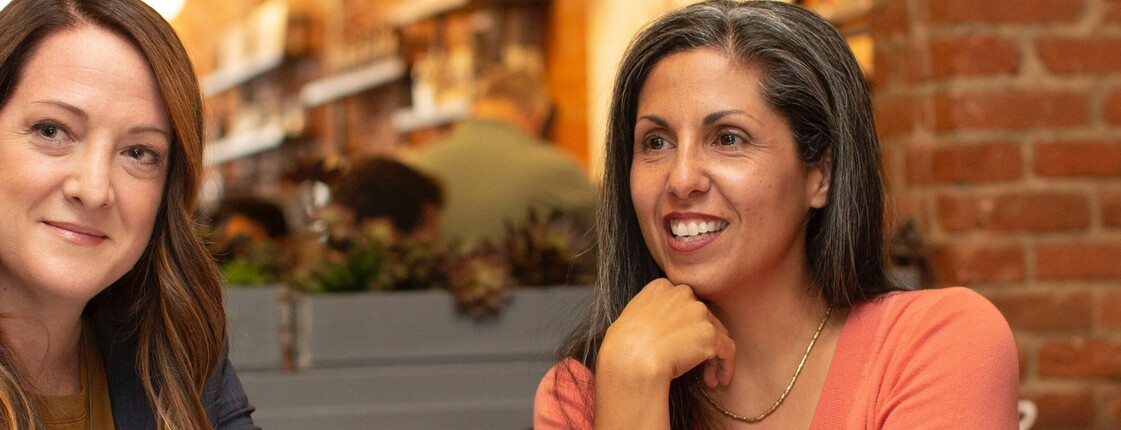 Vier Frauen in Business Kleidung sitzen in einem Café und unterhalten sich.