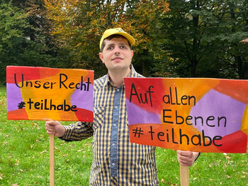 Ein Mann mit gelber Kappe hält zwei Schilder in der Hand. 