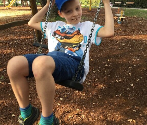 Ein Kind schaukelt auf einem Spielplatz im Donaupark. Im Hintergrund sind weitere Spielgeräte und Bäume zu sehen.