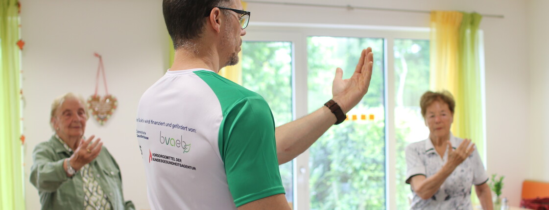 Ein Sportwissenschafter macht Bewegungsübungen mit zwei Seniorinnen.