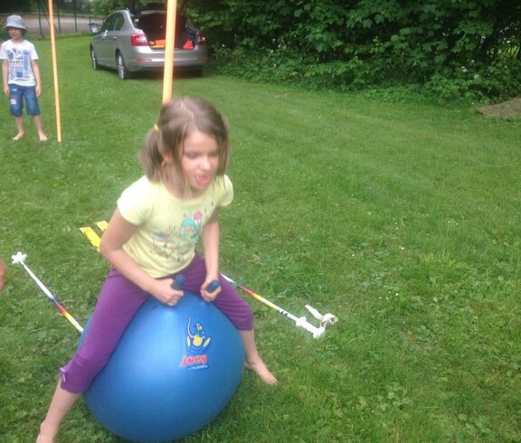 Ein Kind sitzt auf einem großen Hüpfball auf einer Wiese und nimmt während der Projektwoche an spielerischen Bewegungsaktivitäten teil.