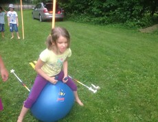 Ein Kind sitzt auf einem großen Hüpfball auf einer Wiese und nimmt während der Projektwoche an spielerischen Bewegungsaktivitäten teil.