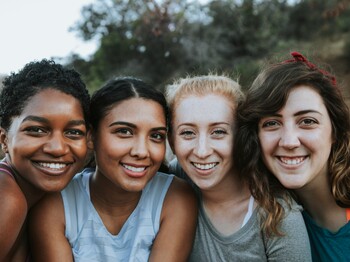 Vier Freundinnen stehen im Freien zu einem Gruppenfoto zusammen.