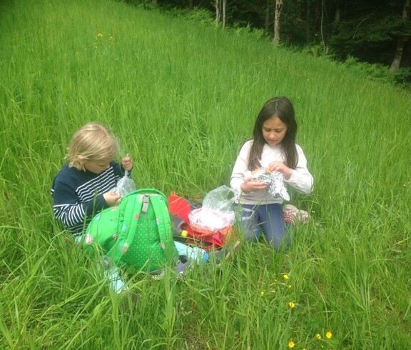 Zwei Kinder sitzen in einer Blumenwiese bei einer Pause im Freien und genießen während der Projektwoche eine Jause in der Natur.