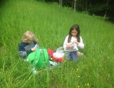 Zwei Kinder sitzen in einer Blumenwiese bei einer Pause im Freien und genießen während der Projektwoche eine Jause in der Natur.