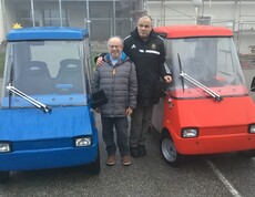 Zwei Männer stehen im Freien zwischen zwei Autos