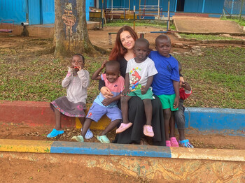 Person sitzt mit mehreren Kindern auf einer bunten Kante im Hof des Nsambya Babies Home.