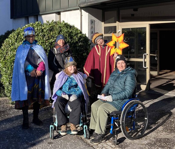 Drei Sternsinger mit Begleitung, zwei Personen im Rollstuhl.