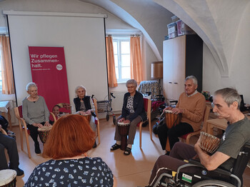 Bewohner*innen sitzen im Kreis und musizieren mit Trommeln bei einer Bewegungs- und Musikrunde im Haus Michael.