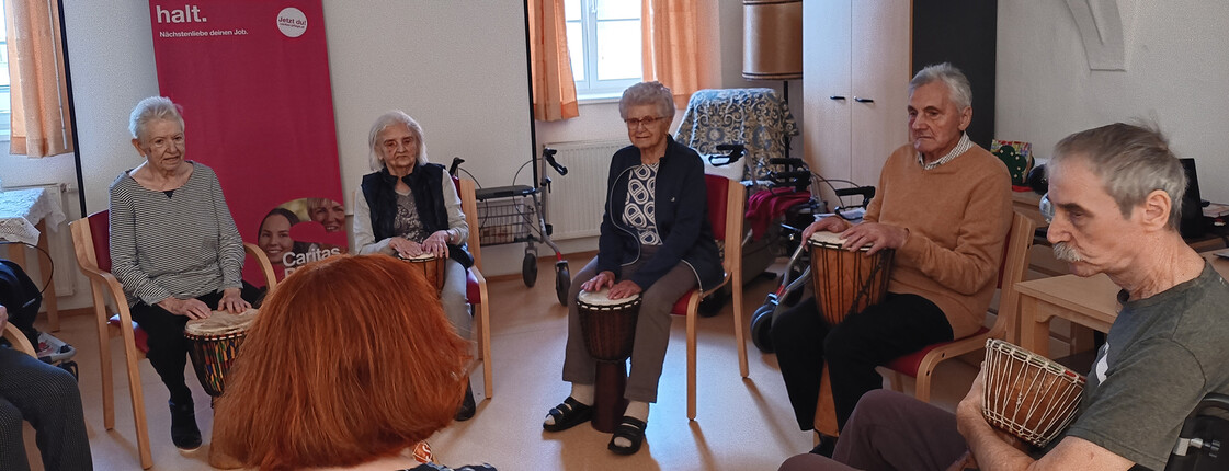Bewohner*innen sitzen im Kreis und musizieren mit Trommeln bei einer Bewegungs- und Musikrunde im Haus Michael.