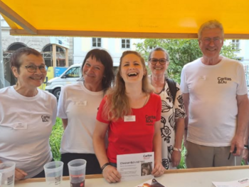 Fünf Personen stehen im Freien hinter einem Informationstisch und lächeln in die Kamera