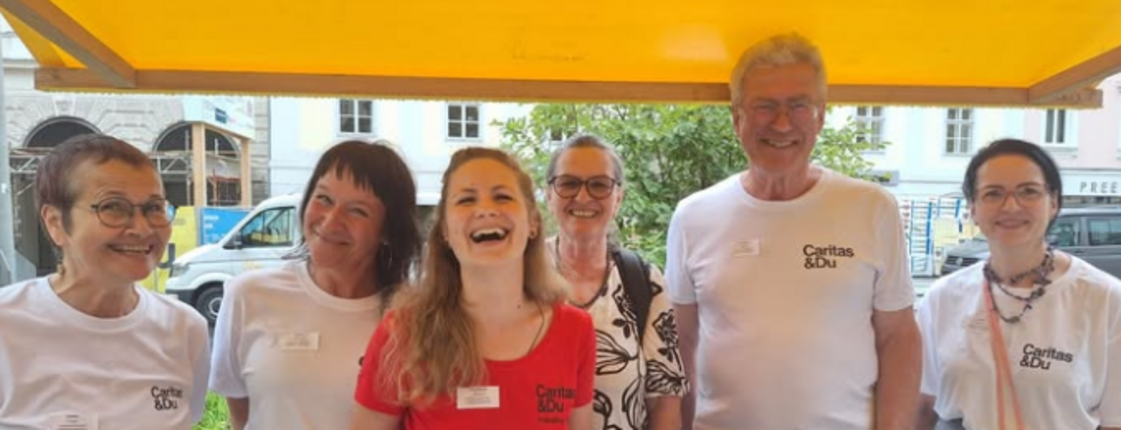 Fünf Personen stehen im Freien hinter einem Informationstisch und lächeln in die Kamera