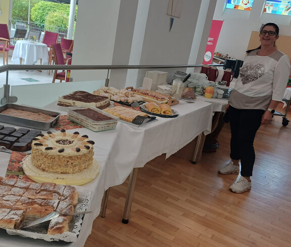 Frau präsentiert ein großes Kuchenbuffet mit Torten, Strudel und Mehlspeisen beim Herbstfest.