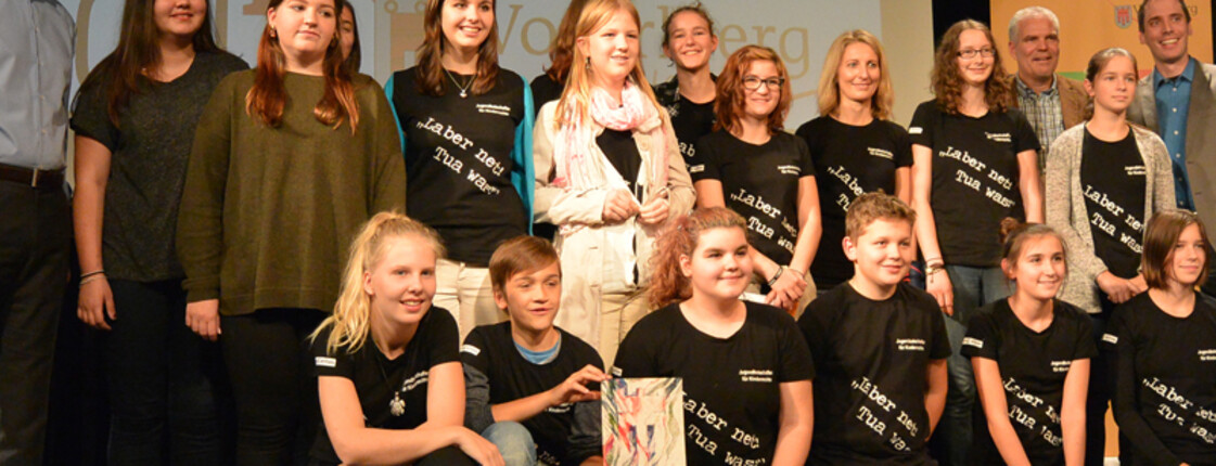 Jugendliche stehen mit Landeshauptmann Markus Wallner auf einer Bühne. Sie trägen alle schwarze T-Shirts mit einer weißen Schrift. 