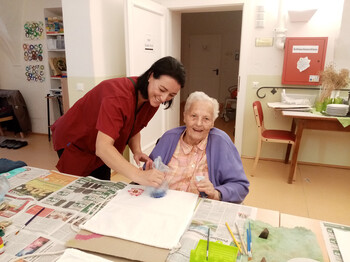 Seniorin und Pflegekraft bemalen gemeinsam eine Stofftasche im Pflegewohnhaus Haus Michael.