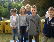 Mehrere Kinder stehen bei einer Gruppenaktivität auf einer Plane im Freien und nehmen gemeinsam an einem Team- und Geschicklichkeitsspiel teil.