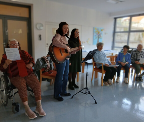 Zwei Personen musizieren mit Gitarre, Gruppe hört zu, Adventfeier im Gemeinschaftsraum