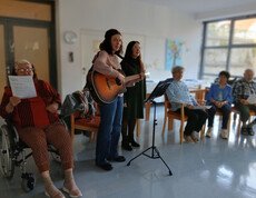 Zwei Personen musizieren mit Gitarre, Gruppe hört zu, Adventfeier im Gemeinschaftsraum