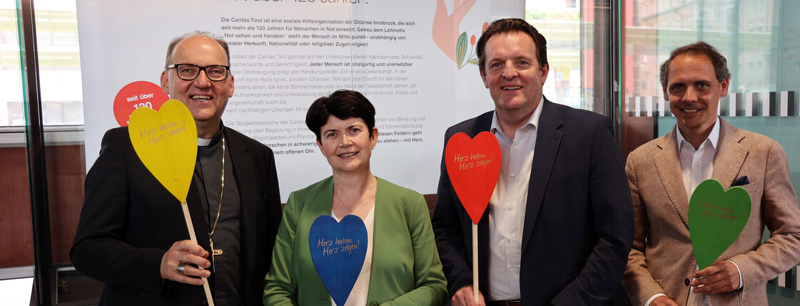 Vier Menschen sind zu sehen, die bunte Holzherzen in den Händen haben.