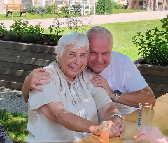 Zwei Personen sitzen eng beieinander an einem Tisch im Garten des Pflegewohnhauses während des Grillfests.