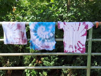 Auf einer Wäscheleine hängen drei bunte T-Shirts in der Schulsozialarbeit gefertigt