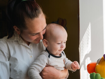 Eine junge Mutter hält ihr kleines Baby liebevoll in den Armen und lächelt ihm zu.