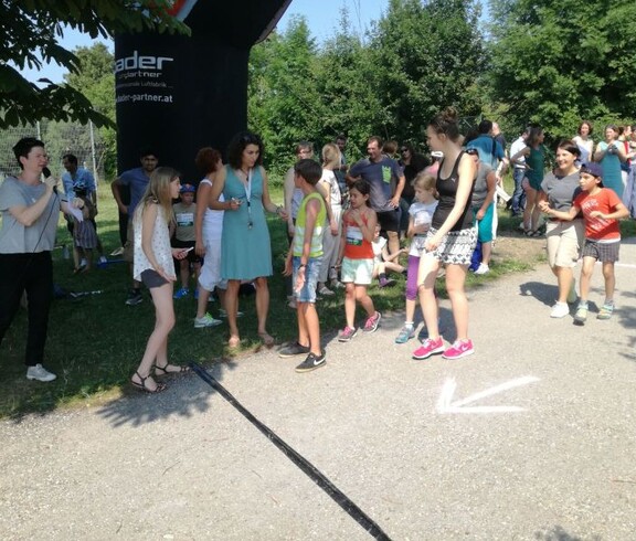Kinder und Begleitpersonen versammeln sich an der Laufstrecke einer Sportveranstaltung und verfolgen gemeinsam das Geschehen.