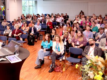 Ein Blick in einem vollgefüllten Saal, wo die Menschen auf Stühlen sitzen.