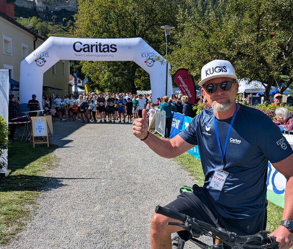 Michi Fixl, als Organisator, auf Fahrrad vor dem Startbogen, dahinter warten zahlreiche Läufer*innen auf den Start.
