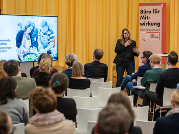 eine Frau steht vor Menschen die auf Sessel sitzen