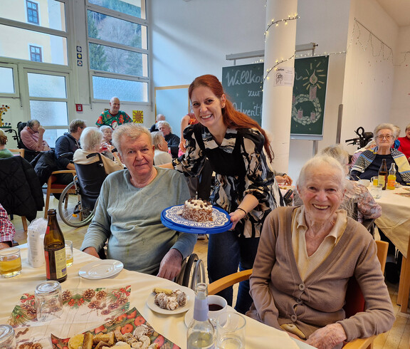 Person präsentiert Kuchen an zwei Gäste, festlich gedeckter Tisch im Pflegewohnhaus