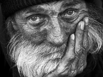 Älterer Mann mit Bart und Mütze blickt ernst in die Kamera, stützt das Gesicht auf seine Hand