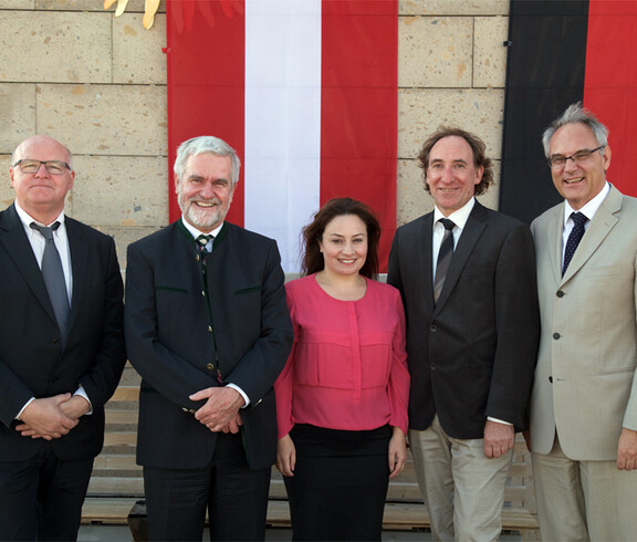 Ein Gruppenfoto zeigt fünf bekannte Personen. Im Hintergrund befindet sich eine Österreichflagge.