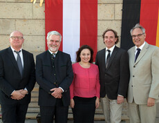 Ein Gruppenfoto zeigt fünf bekannte Personen. Im Hintergrund befindet sich eine Österreichflagge.