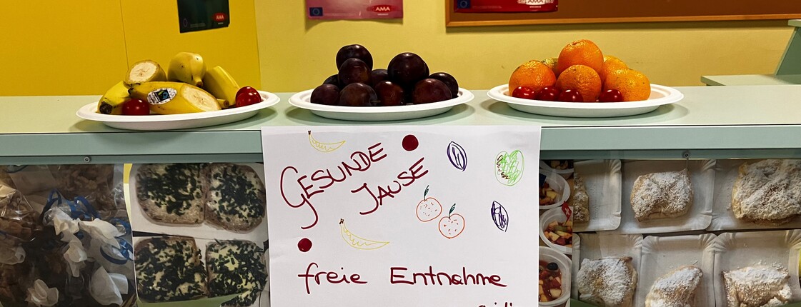 Die "Gesunde Jause"  wurde in der Schule aufbereitet, auf drei Tellern liegt Obst und Gemüse, darunter ein Schild mit gezeichnetem Obst und Gemüse und der Aufschrift "Gesunde Jause, Freie Entnahme"