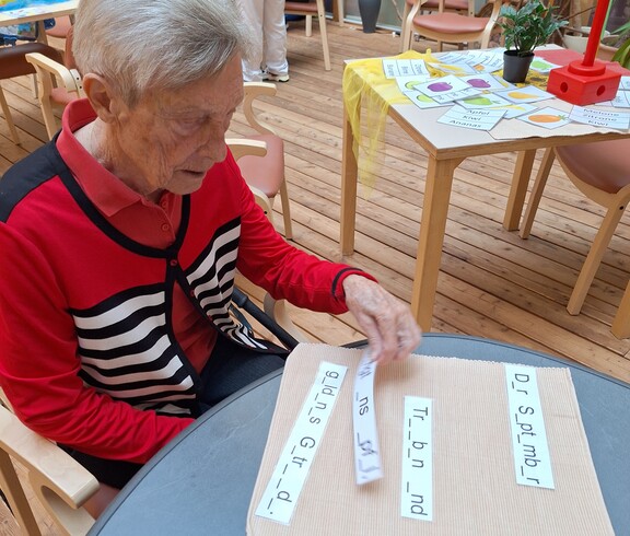 Eine Bewohnerin des Pflegewohnhauses nimmt im Rahmen des Tags der Demenz an einer Gedächtnisübung teil und ordnet Wortkarten an einem Tisch zu, während im Hintergrund weitere Mitmachstationen zu sehen sind.