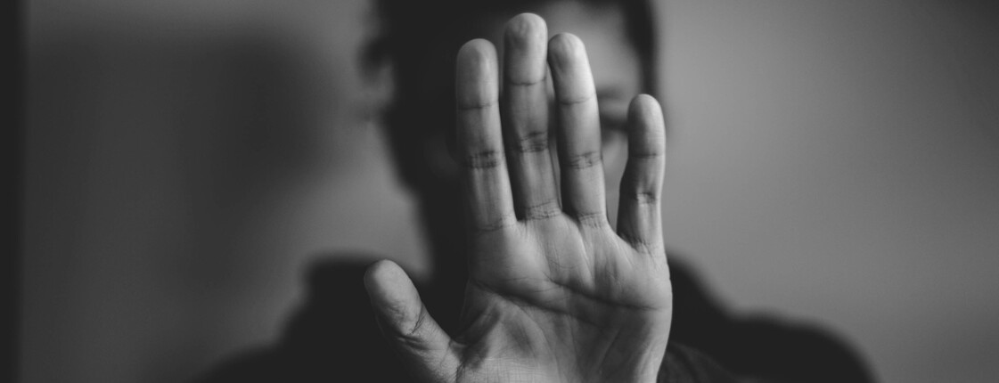 Das schwarz-weiß Foto zeigt eine Frau, die als Abwehrhaltung ihren Arm der Kamera entgegen streckt.