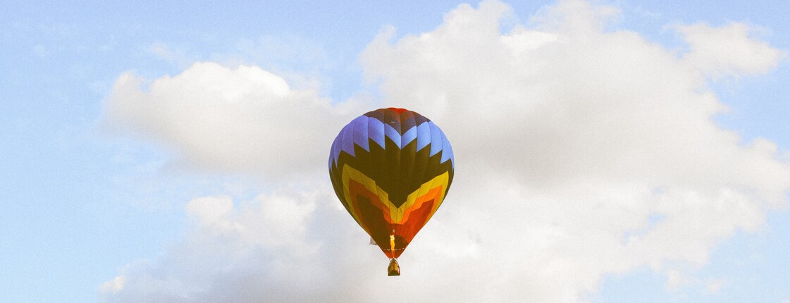 Zwei Heißluftballons schweben vor einem blauen Himmel mit weißen Wolken. Die Aufnahme vermittelt Weite, Ruhe und Leichtigkeit.
