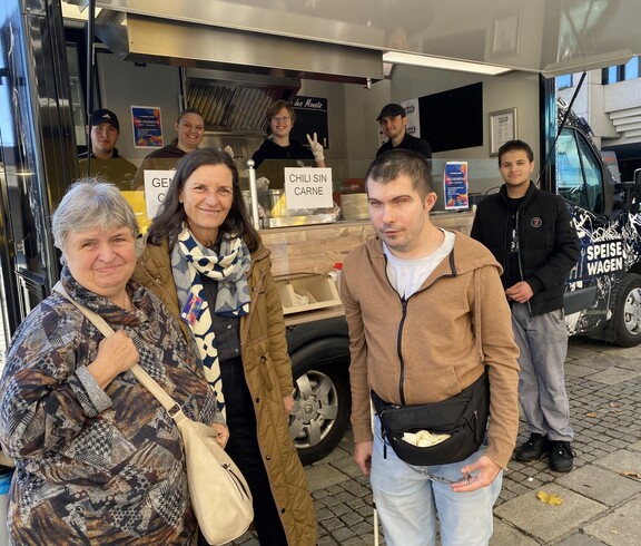 Mitglieder der Inklusiven Redaktion und SOB-Leitung Conny Zefferer vor dem Speisewagen der Caritas OÖ beim Inklusionstag der Stadt Linz 2025