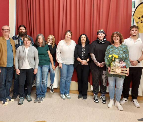 Gruppenfoto von mehreren Personen in einem Raum im Hintergrund ein roter Vorhang.